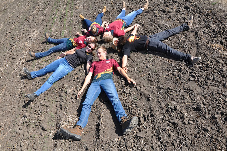 Six students lying on soil in a ring, with hands joined to make a star shape.