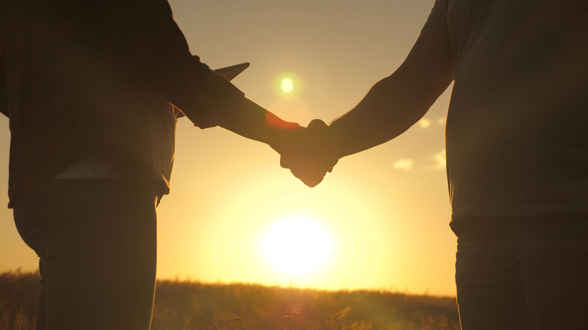 Silhouette of two people shaking hands with the sun setting behind