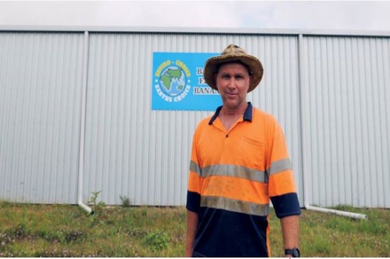 Man wearing hat standing in front of shed with sign on exterior wall.